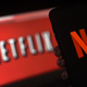 The Netflix red "N" on a phone is shown with the company's older white on red logo in background.